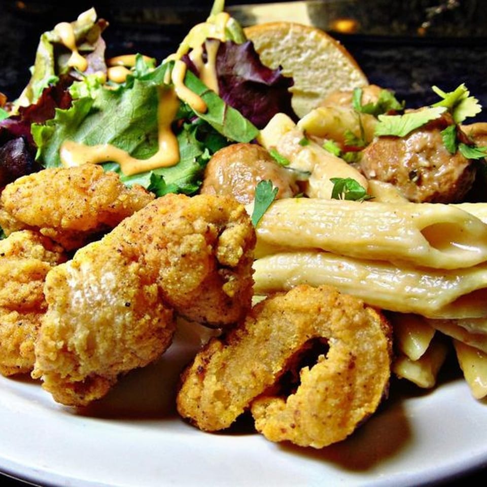 A plate of fried chicken, pasta, meatballs, and a side salad with dressing.