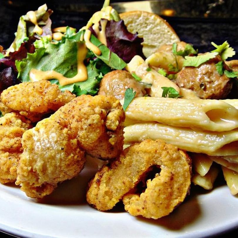 A plate of fried chicken, pasta, meatballs, and a side salad with dressing.
