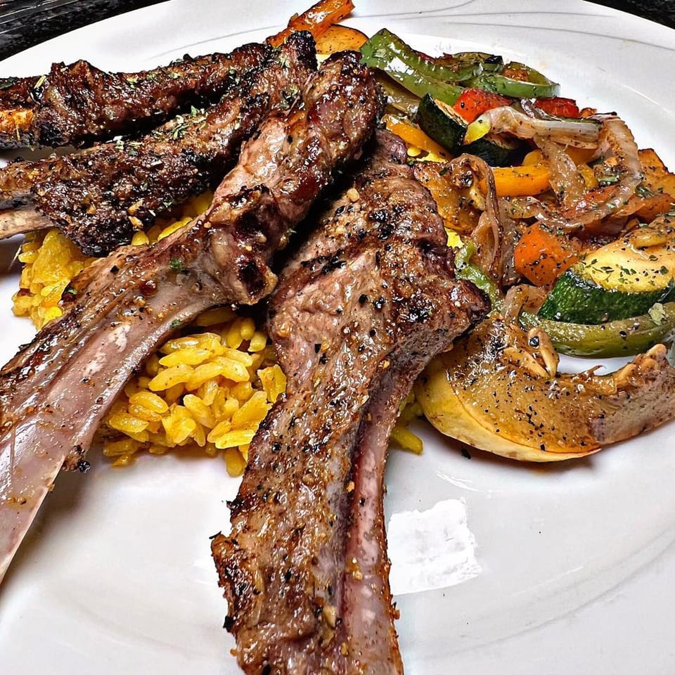 Grilled lamb chops with yellow rice and roasted vegetables on a white plate.