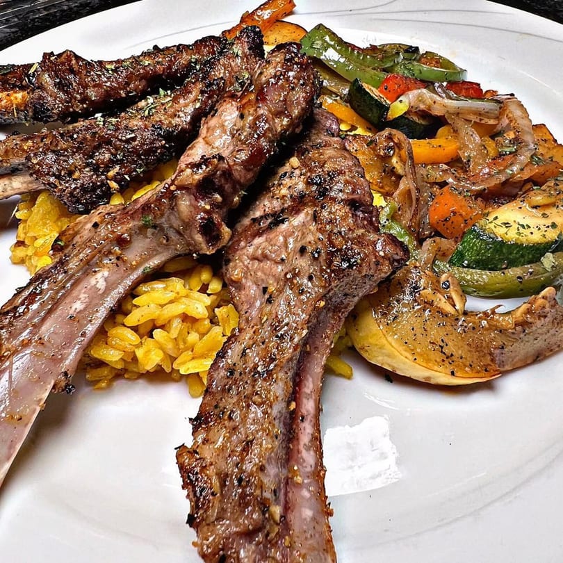Grilled lamb chops with yellow rice and roasted vegetables on a white plate.