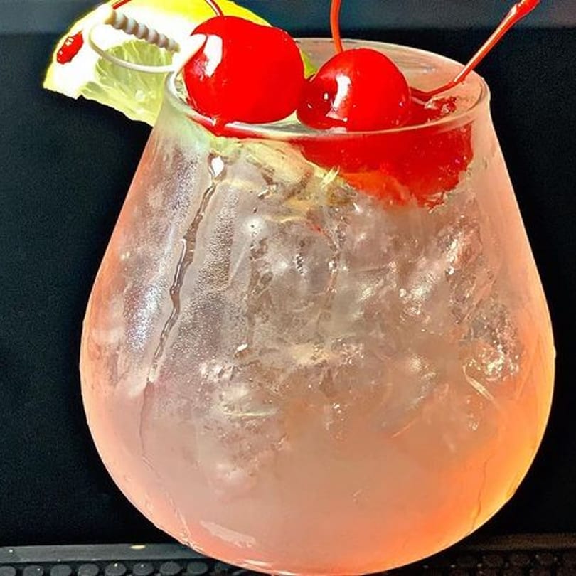 A Kulture Ultra Lounge cocktail with cherries and a lemon slice in a rounded glass.