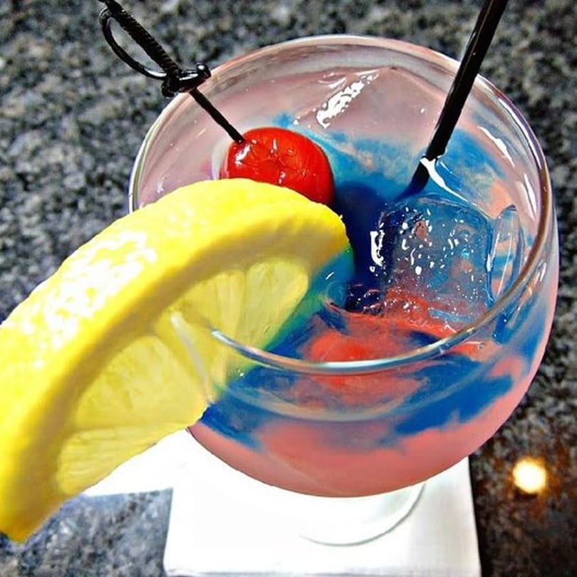 A vibrant red and blue cocktail with a lemon slice and cherry garnish, served at Kulture Ultra Lounge.
